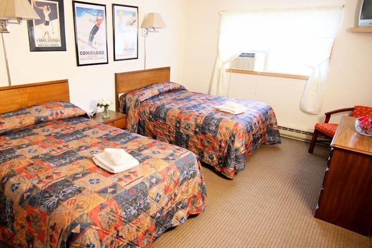 A hotel room with two beds, a desk, a chair, and a TV on a stand.