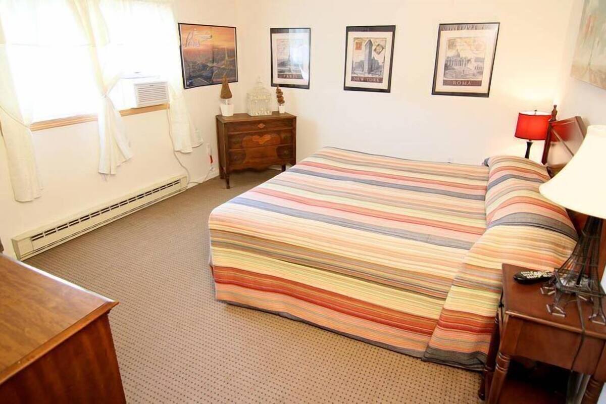 A hotel room with a striped bedspread, a wooden nightstand, a lamp, and framed pictures on the wall.