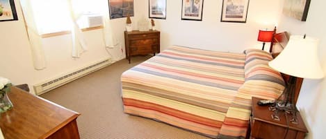 A hotel room with a striped bedspread, a wooden nightstand, a lamp, and framed pictures on the wall.