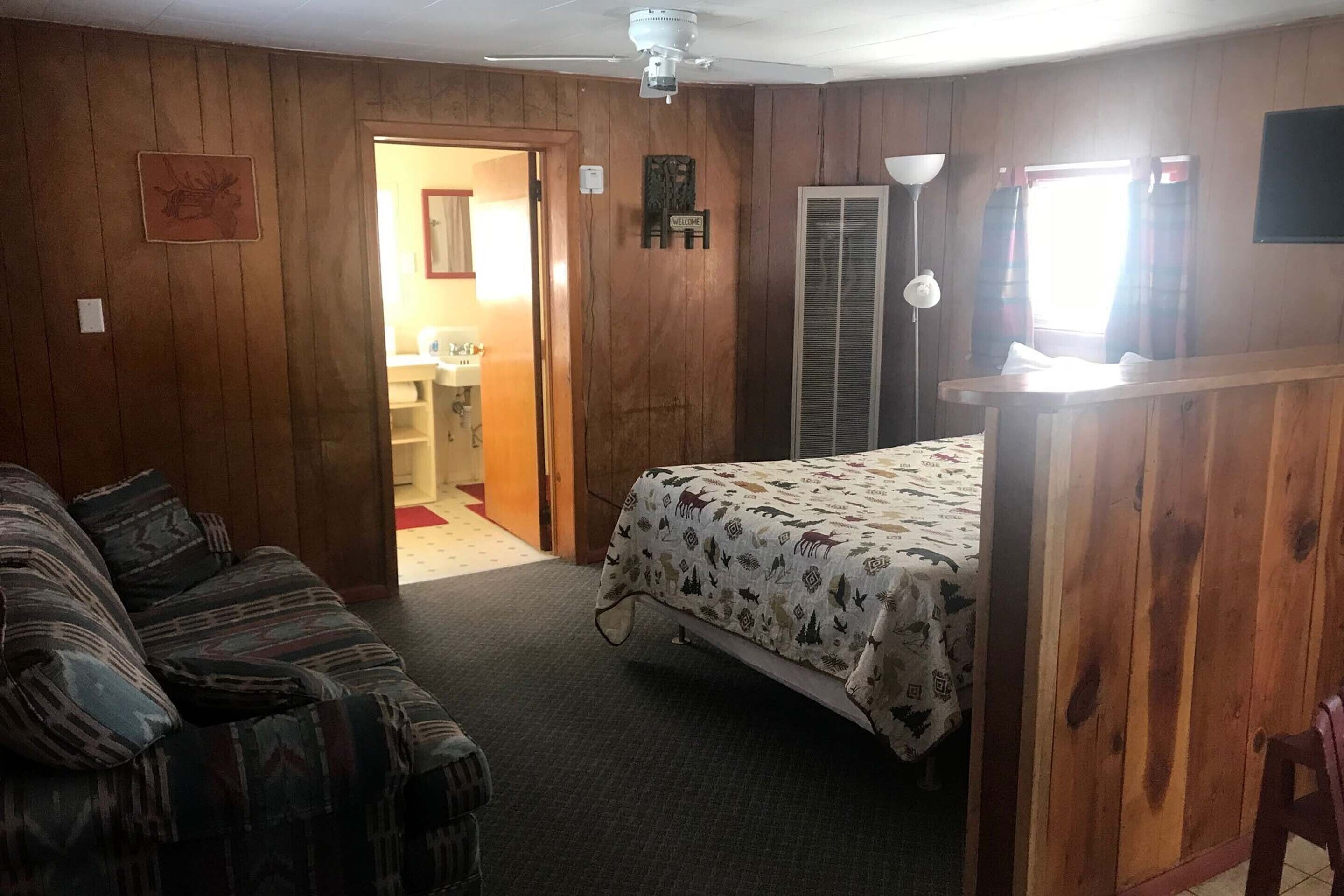 A room with a bed, a couch, a door leading to a bathroom, and a ceiling fan.