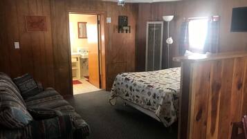 A room with a bed, a couch, a door leading to a bathroom, and a ceiling fan.