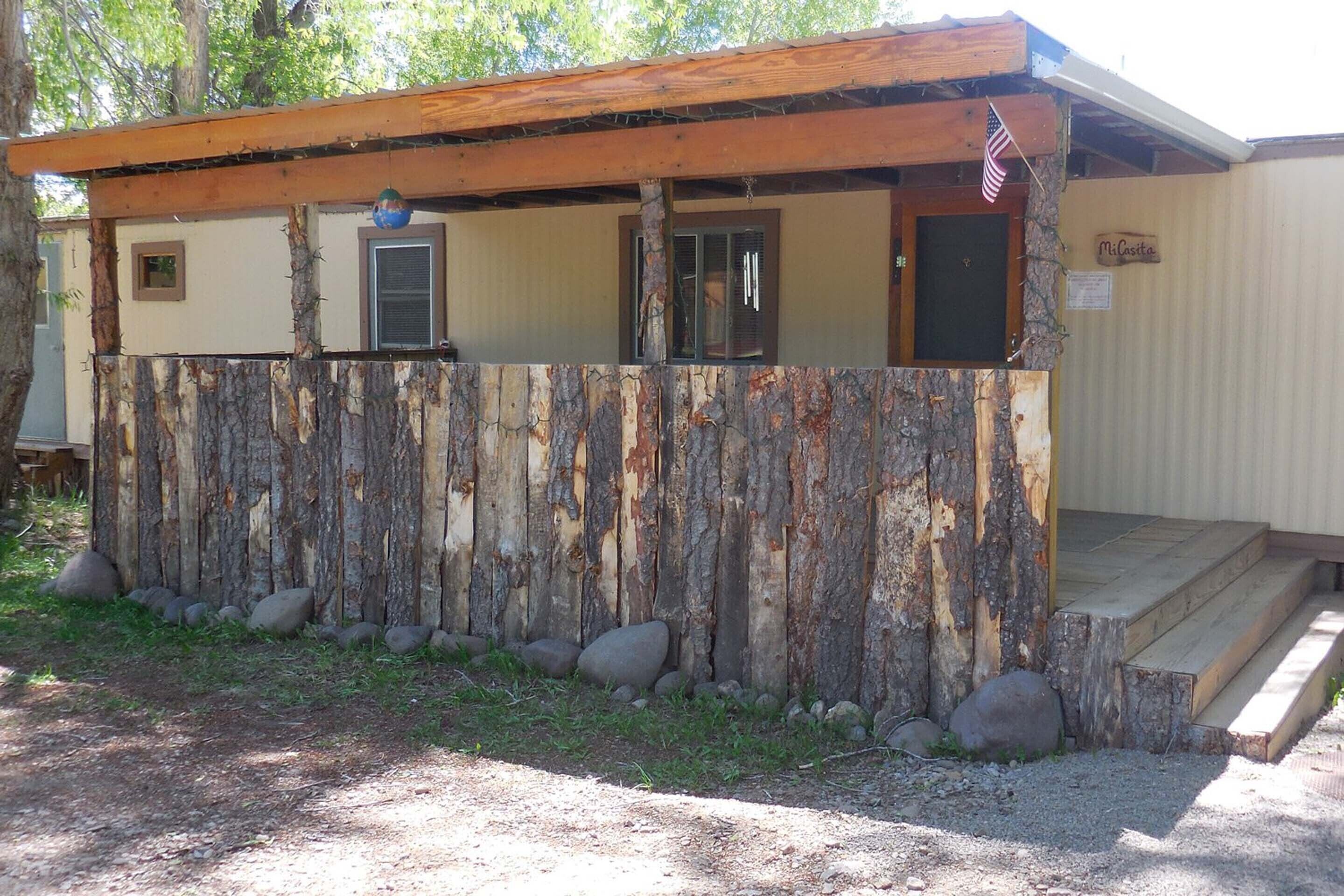 A rustic cabin with a wooden porch, a small front door, and a visible American flag.