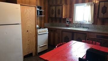 A kitchen with wooden cabinets, a white refrigerator, a stove, a sink, and a red table.
