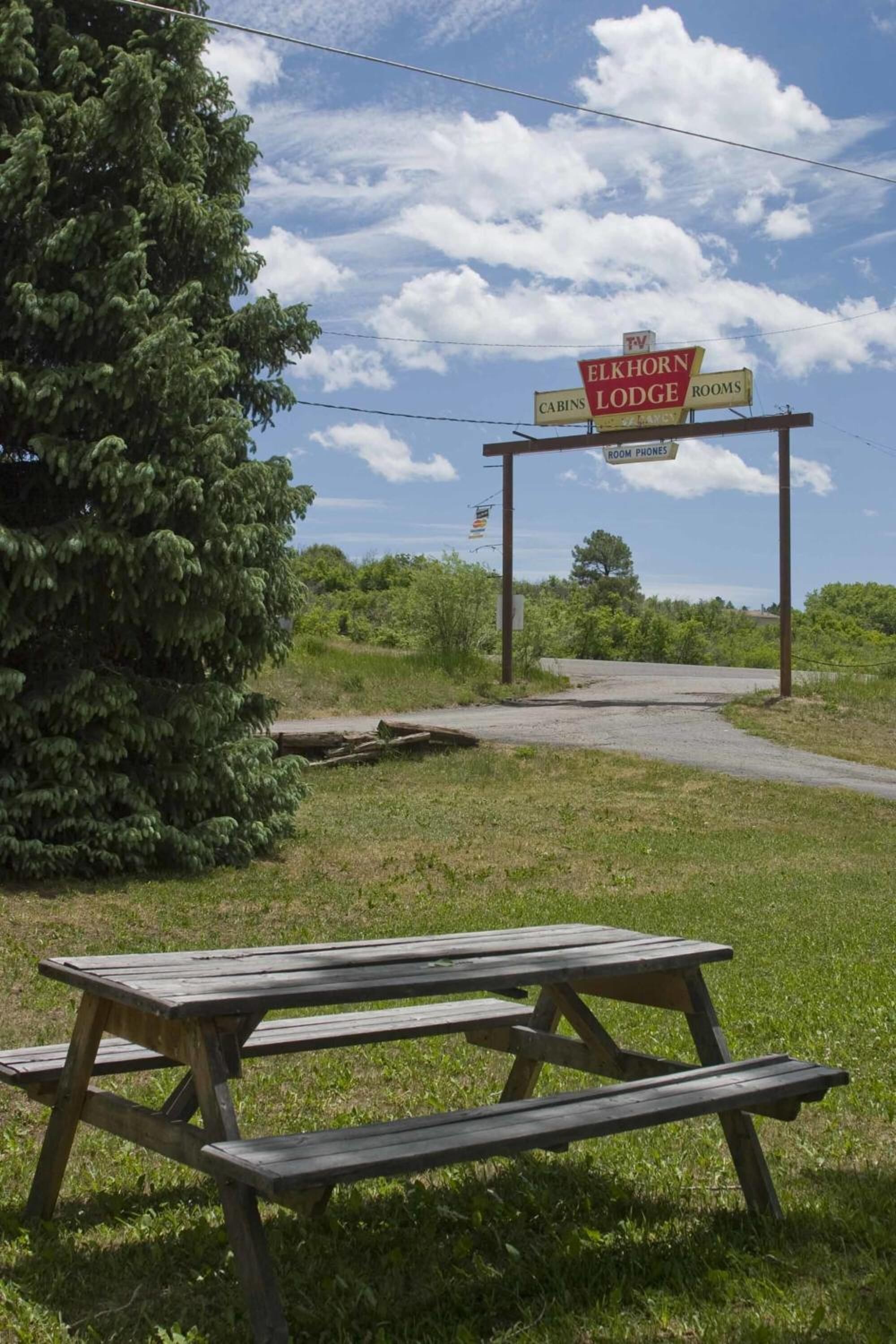 Une table de pique-nique se trouve devant un panneau indiquant l’emplacement d’Elkhorn Lodge, avec la mention que des chalets et des chambres sont disponibles.