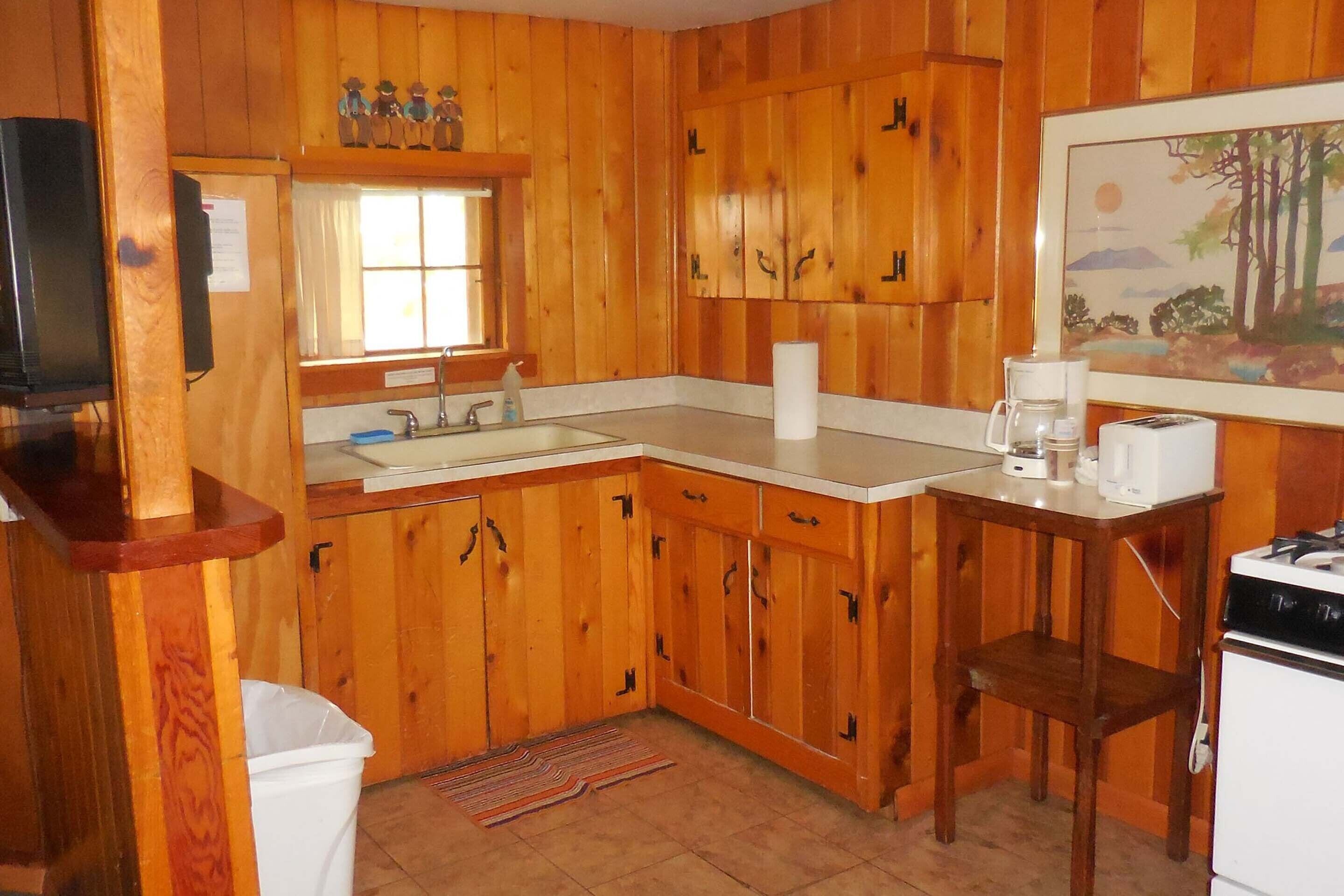 A wooden-paneled kitchen with a sink, stove, and a painting on the wall.