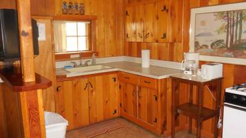 A wooden-paneled kitchen with a sink, stove, and a painting on the wall.