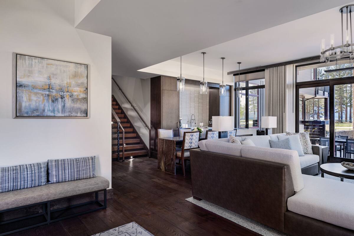 A spacious living room with a large sofa, a dining area, and a staircase leading to an upper level.