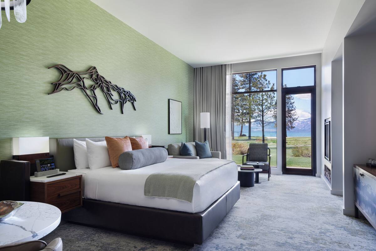 A modern hotel room with a large bed, a desk, a chair, and a view of the outdoors.