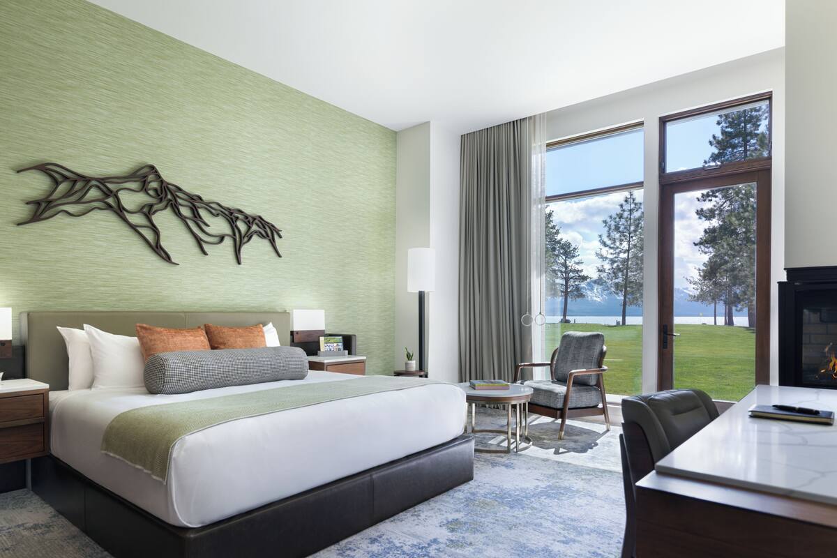 A hotel room with a large bed, a desk, a chair, a TV, and a view of a lake.