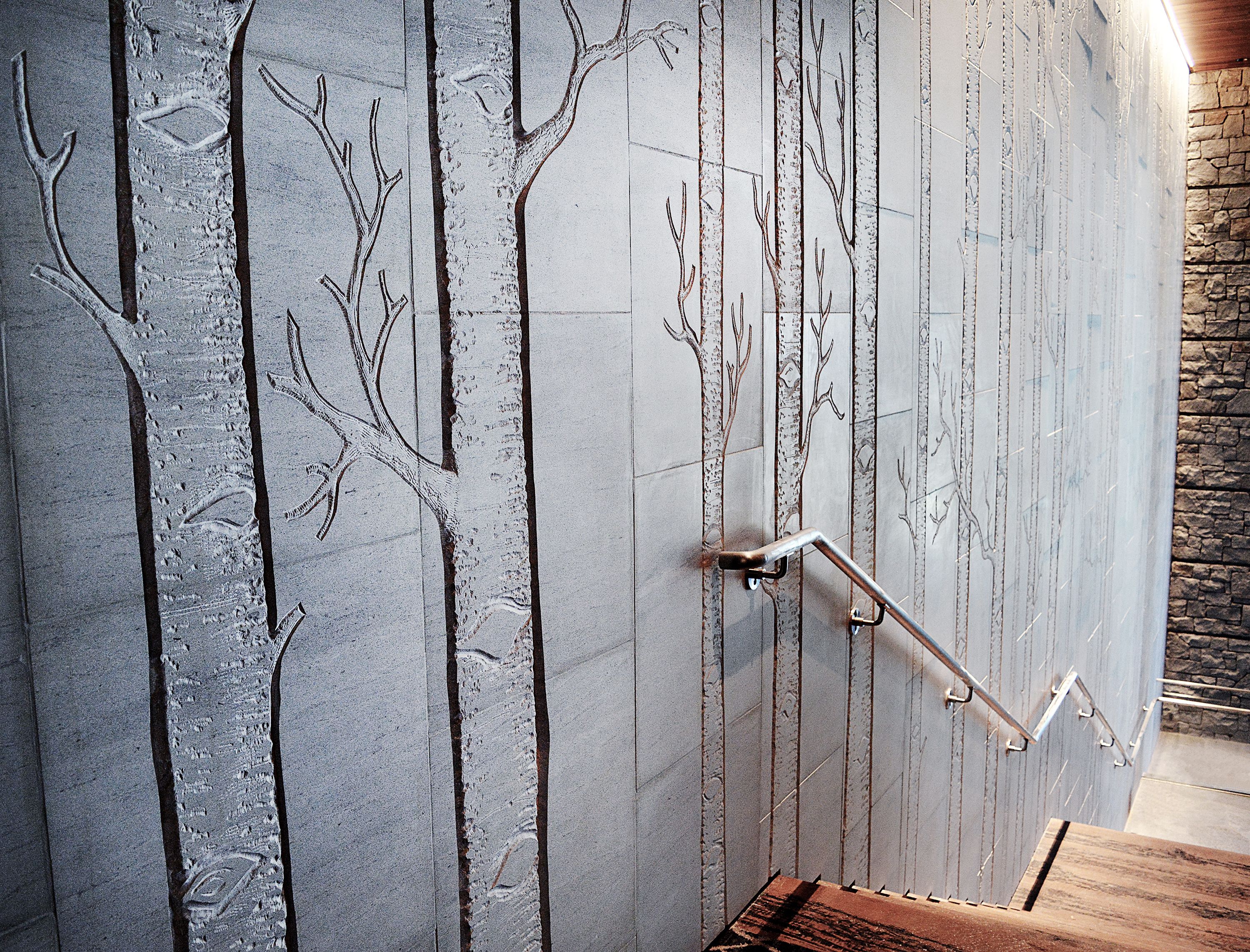 A bathroom with a stone wall featuring tree and branch designs, a wooden bench, and a stone wall adjacent to the bathroom.