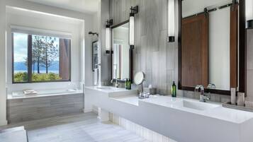 Un baño moderno con dos lavamanos, un espejo grande y una ventana con vistas a árboles y montañas.
