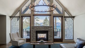Amplia sala de estar con chimenea de piedra, ventanas grandes con vistas a la montaña y una lámpara moderna.