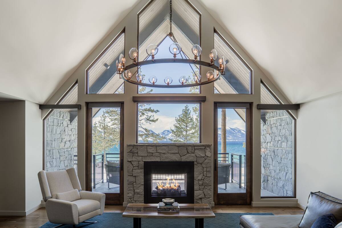 A spacious living room with a stone fireplace, large windows offering mountain views, and a modern chandelier.