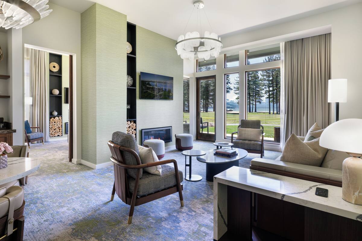A spacious living room with a fireplace, comfortable seating, a coffee table, and large windows offering a view of the outdoors.