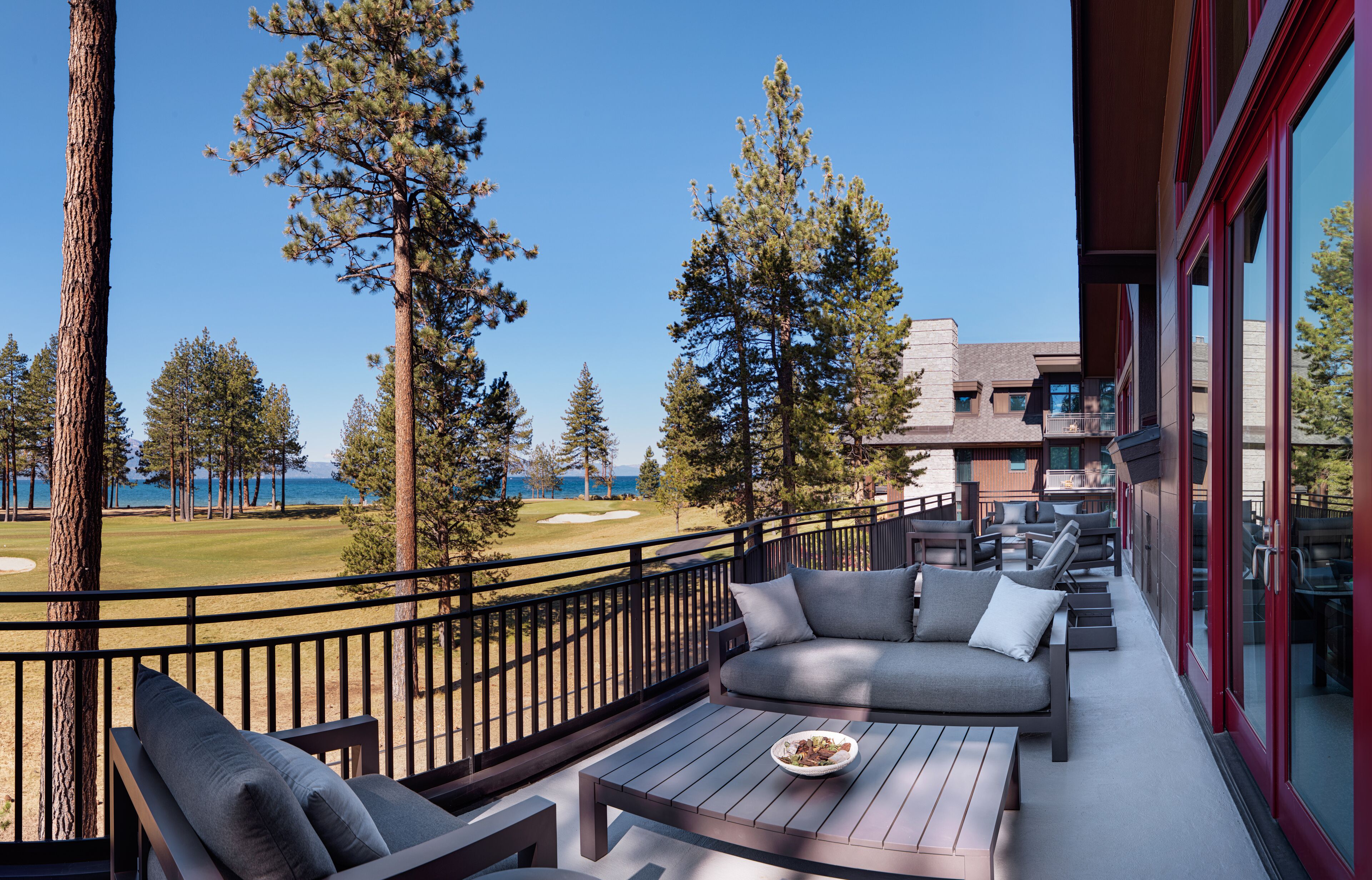 A balcony with a view of a golf course, outdoor seating, and a dining table.