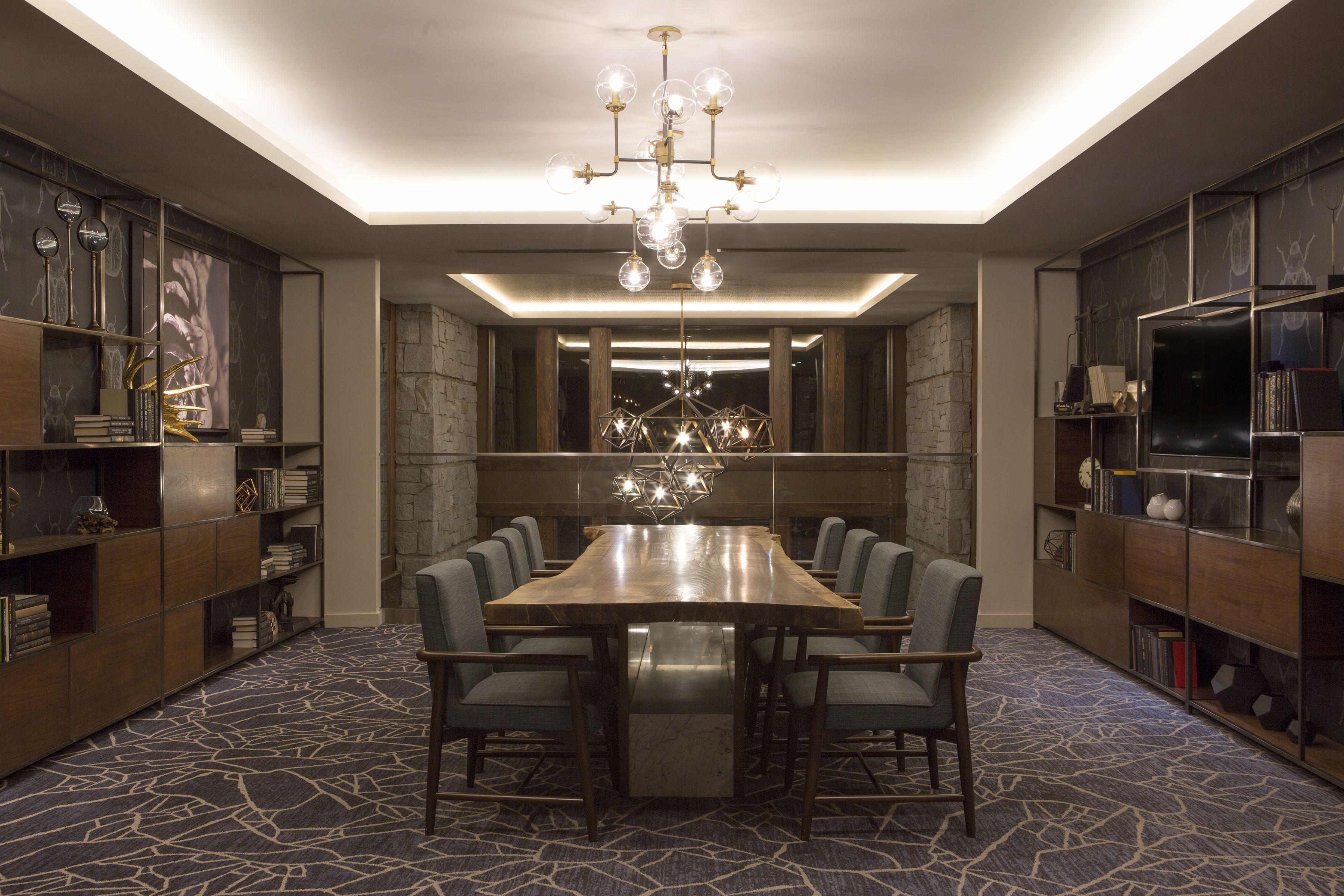 A conference room with a large table, chairs, a chandelier, bookshelves, and a patterned carpet.