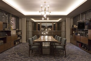 A conference room with a large table, chairs, a chandelier, bookshelves, and a patterned carpet.