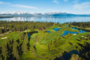 A golf course with multiple ponds, surrounded by dense forests and mountains in the background.