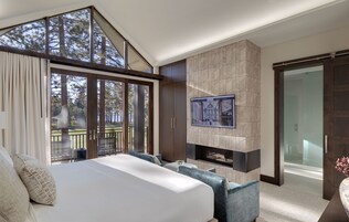 Un dormitorio moderno con una cama grande, una chimenea y un balcón con vistas a árboles.