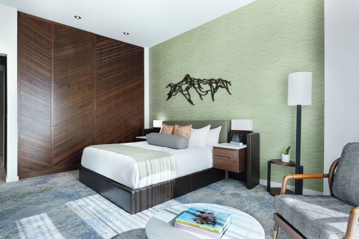 A modern hotel room with a large bed, a nightstand, a chair, a lamp, and a wall art piece.