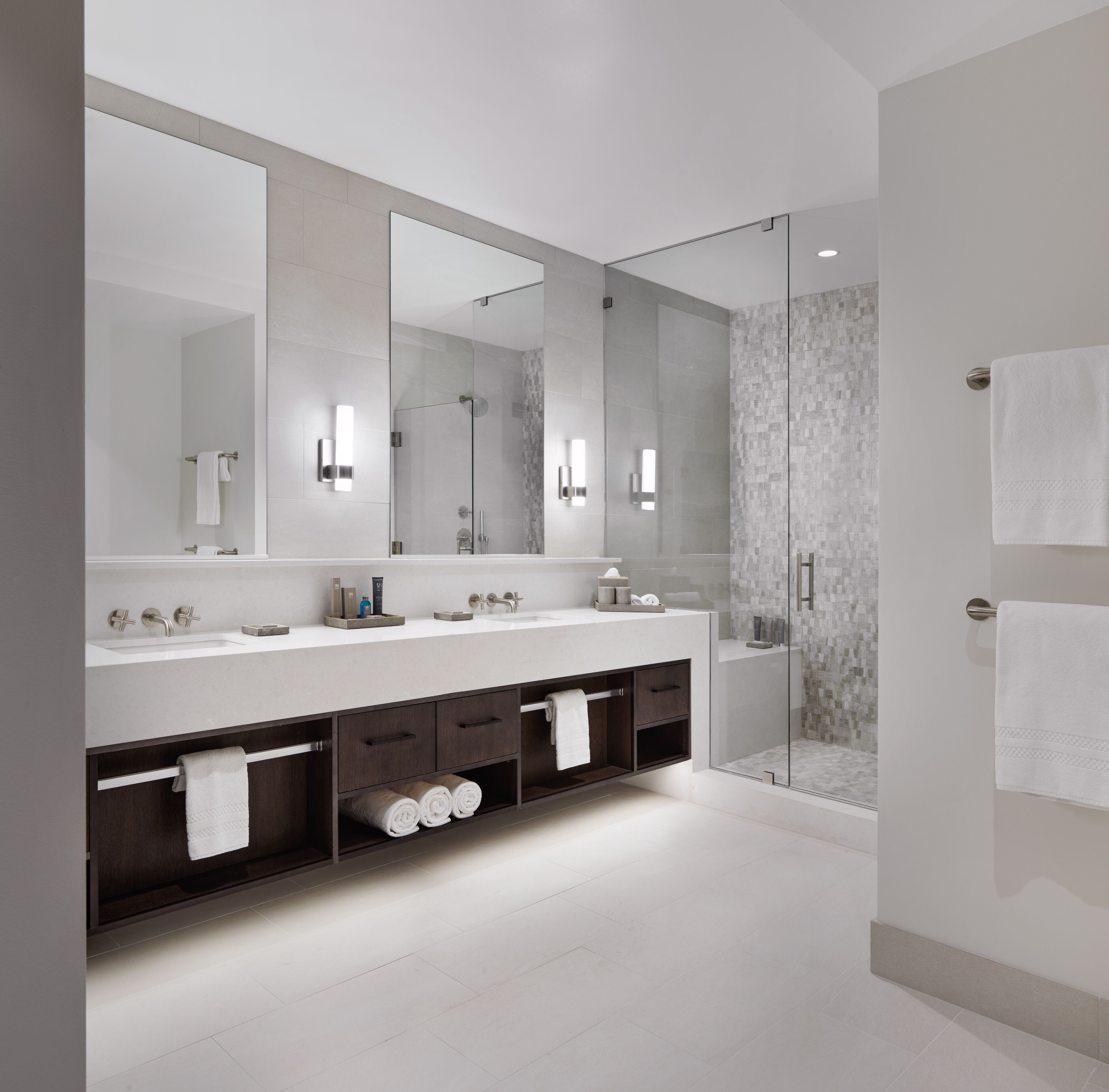 A modern bathroom with a large mirror, two sinks, a shower, and built-in shelves.