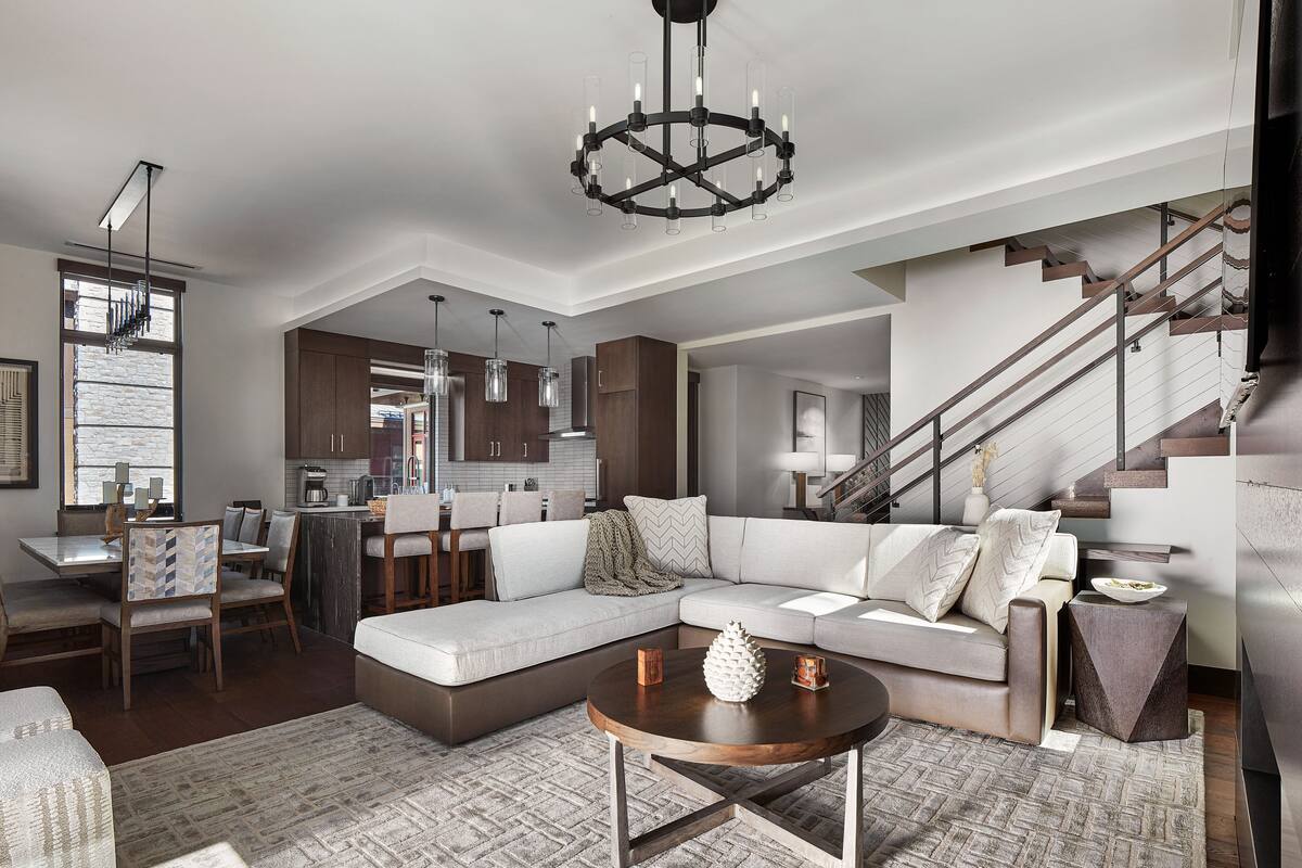 A spacious living area with a sectional sofa, a round coffee table, and a staircase.