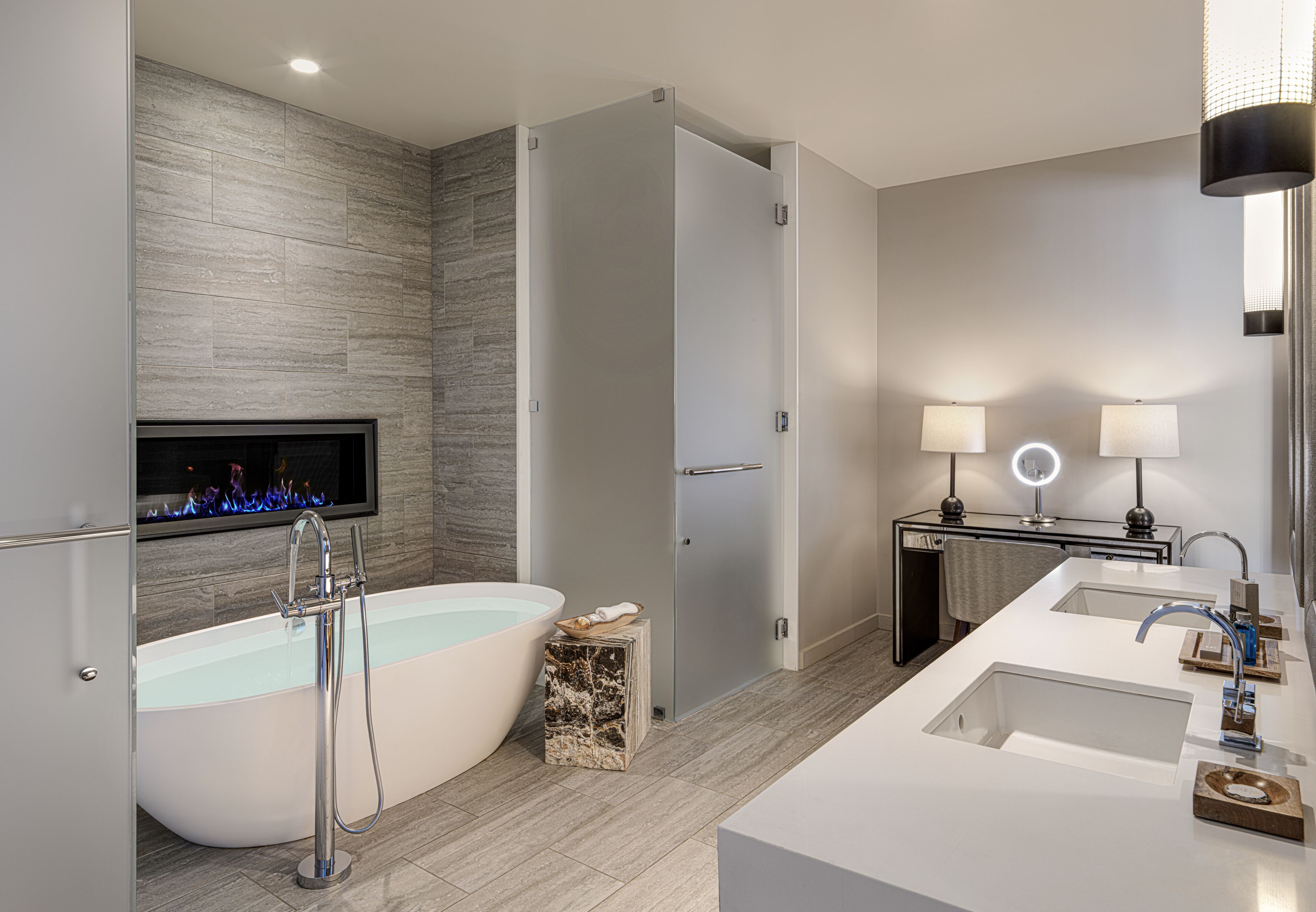 Un baño moderno con una bañera independiente, un tocador con dos lavamanos y un televisor montado en la pared.