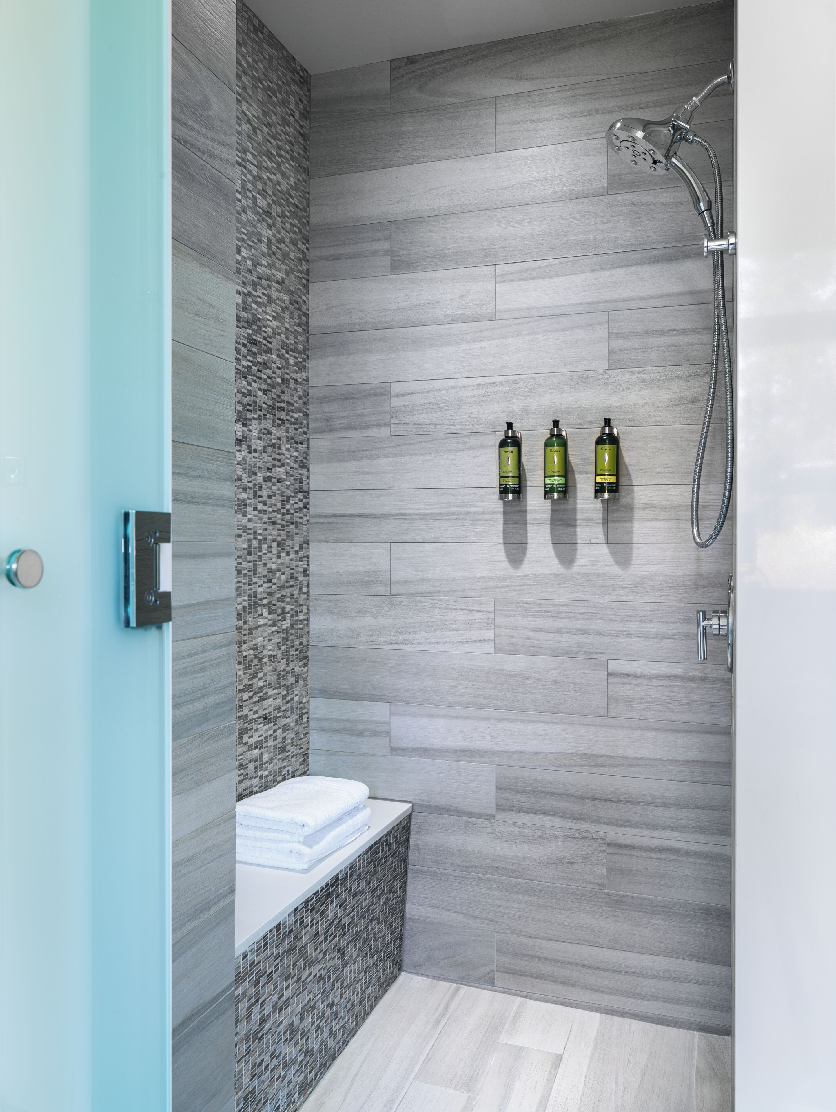 Ein modernes Badezimmer mit Dusche, Fliesenwand und drei Shampoo-Flaschen.