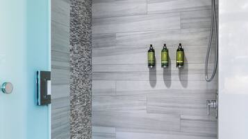 Ein modernes Badezimmer mit Dusche, Fliesenwand und drei Shampoo-Flaschen.