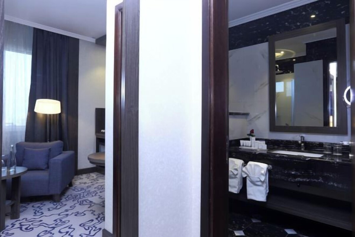 A hotel room with a seating area, a large mirror, a black marble sink, and a patterned floor.