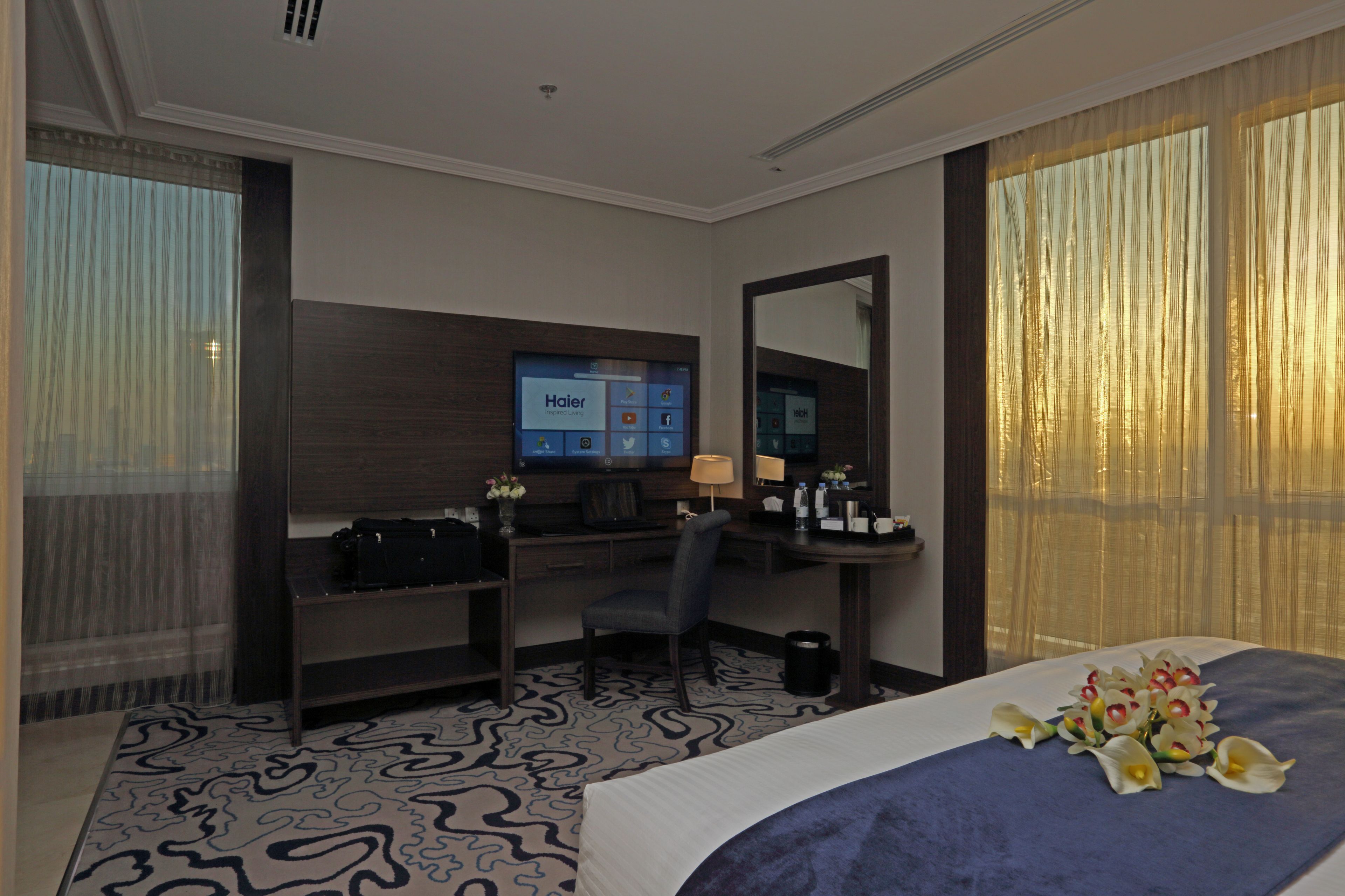 Une chambre d’hôtel avec un lit, un bureau, une chaise, une télévision et une grande fenêtre avec des rideaux.
