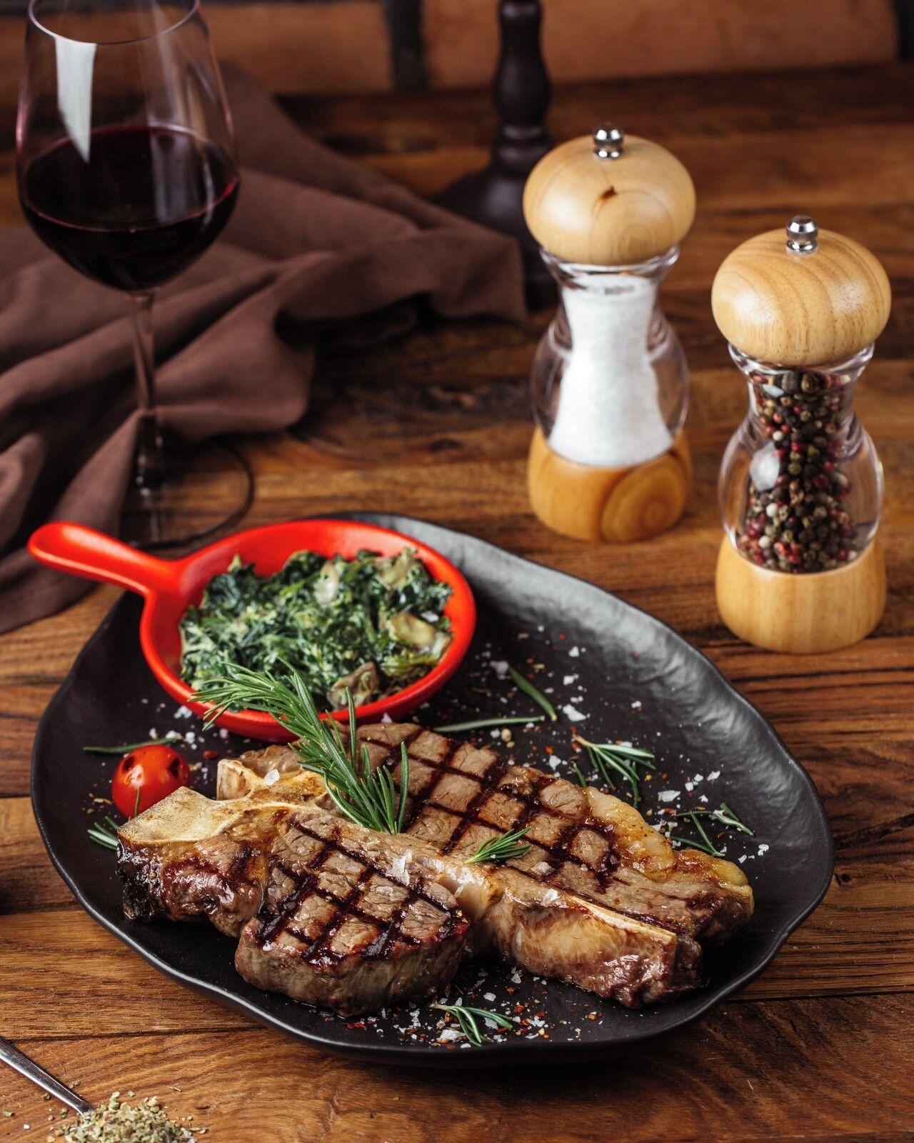 Une assiette de viande grillée, un saladier rouge rempli de légumes verts et un verre de vin rouge sur une table en bois.