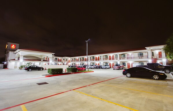 A multi-story motel with a central courtyard, multiple parking spaces, and a well-lit exterior. - Palace Inn Copperfield (Houston)