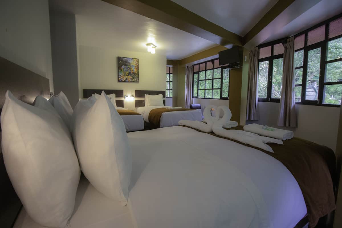 A hotel room with a large bed, two bedside tables, a painting on the wall, and windows with curtains.