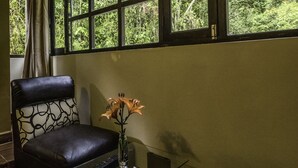 Ein Zimmer mit einem großen Fenster, einem Ledersessel, einem Glastisch und einer Vase mit Blumen.