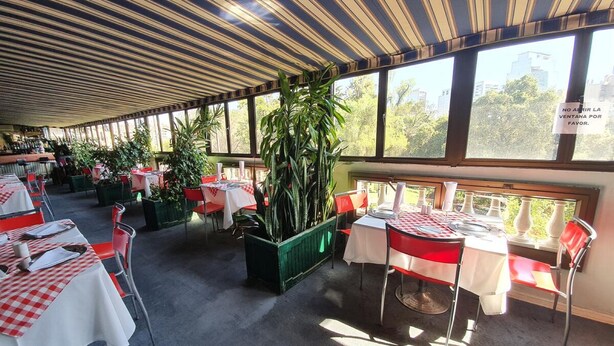 An indoor dining area with tables set for two, large windows, and potted plants. - Foresta Hotel (Santiago)