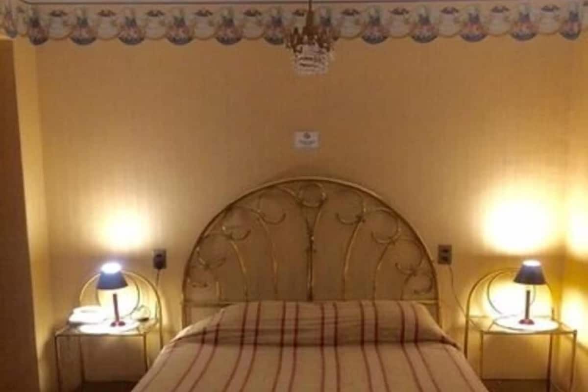 A bed with a striped bedspread, two bedside tables with lamps, a decorative ceiling medallion, and a wall with a floral pattern.
