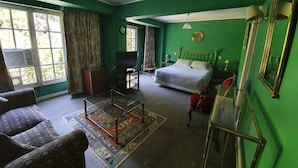 A room with a bed, a television, a desk, and a chair. There is a window with curtains and a view of trees. - Foresta Hotel (Santiago)