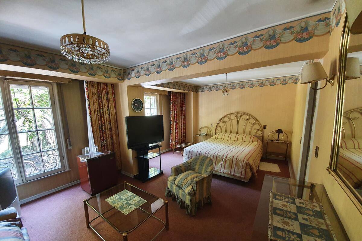 A hotel room with a bed, a television, a sofa, a coffee table, and a chandelier.