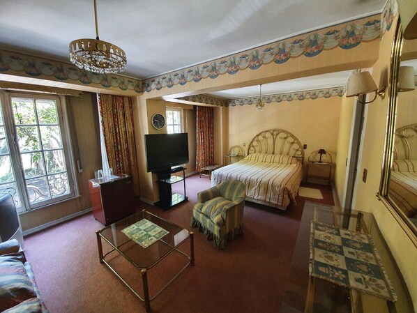 Una habitación de hotel con cama, televisión, sofá, mesa de centro y candelabro.