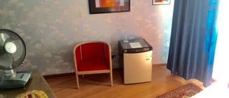 A room with a wooden floor, a red chair, a small table with a fan, a heater, and a patterned rug.