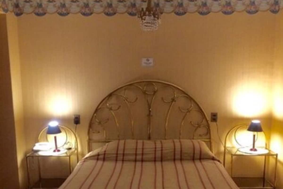 A room with a large bed, two bedside tables, and a chandelier.
