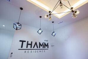 A hotel interior with a modern chandelier, geometric light fixtures, and a prominent sign reading "THAMM RESIDENCE". - THAMM Residence (Nakhon Ratchasima)