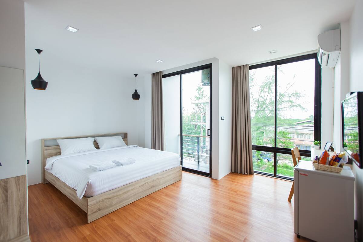 A modern bedroom with a wooden bed, large windows, and a small refrigerator.