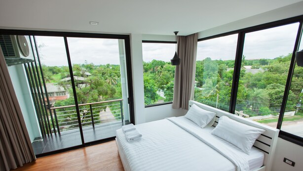A bedroom with a large bed, a view of greenery outside, and a balcony with a railing.