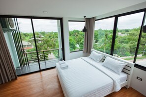 A bedroom with a large bed, a view of greenery outside, and a balcony with a railing. - THAMM Residence (Nakhon Ratchasima)
