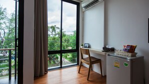 A room with a large window, a desk, a chair, and a small refrigerator.