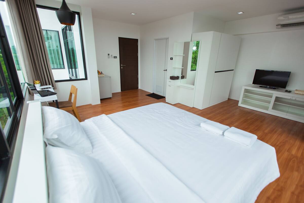 A modern hotel room with a large bed, a desk with a computer, a TV, and a wardrobe.