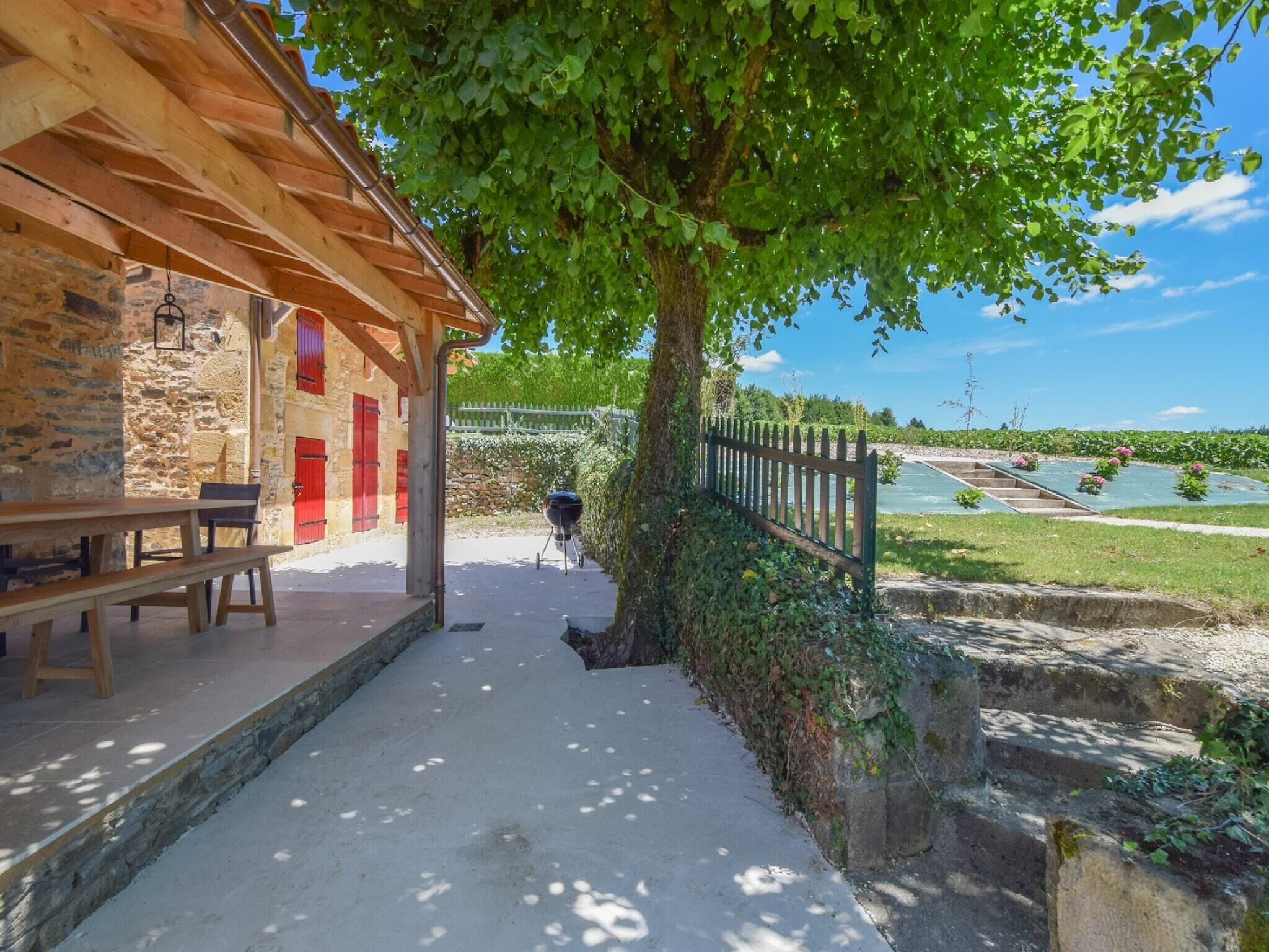 Ein rustikales Steinhaus mit einer Holzpergola, einer Bank und einem Grill vor der Fassade.