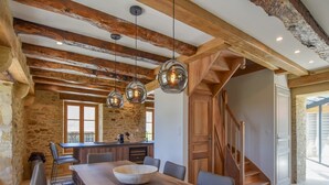 Un coin repas rustique avec une longue table en bois, des bancs et des lampes suspendues.